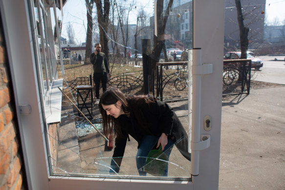 A volunteer cleans the broken glass at a shop which got damaged as a result of shellfire in Kyiv.