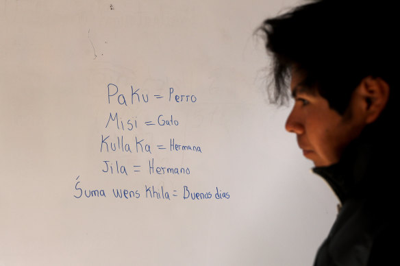 Jose Choque stands next to words he wrote on a school whiteboard in the Uru language.