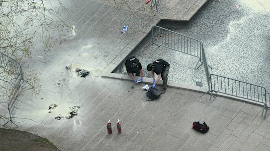 New York Police officers inspect a backpack left at the scene where a man lit himself on fire in a park outside Manhattan criminal court, Friday, April 19, 2024