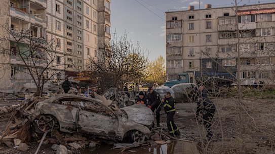 Policemen and emergency personnel check a burned car at the site of the destroyed residential building that was hit during the Russian attack on Uman.