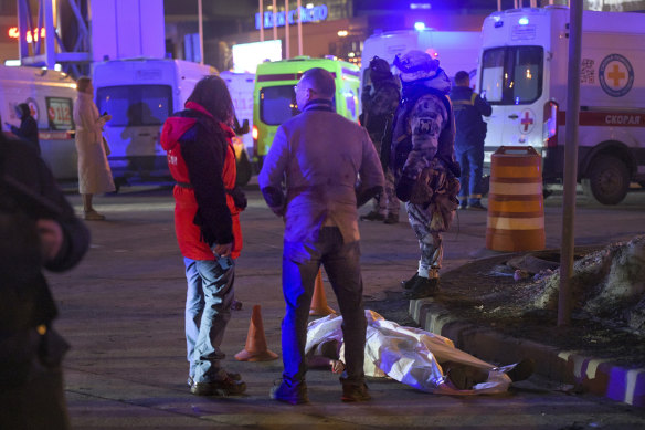 People stand at a body of a victim near the burning building of the Crocus City Hall on the western edge of Moscow.