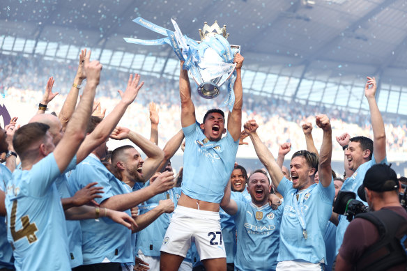 Matheus Nunes holds the Premier League trophy aloft as Manchester City celebrate their title victory.