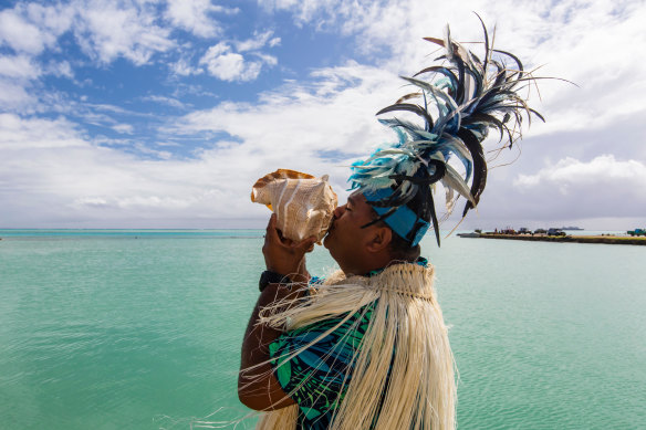 A local blows into a conch shell as he welcomes visitors to Aitutaki.