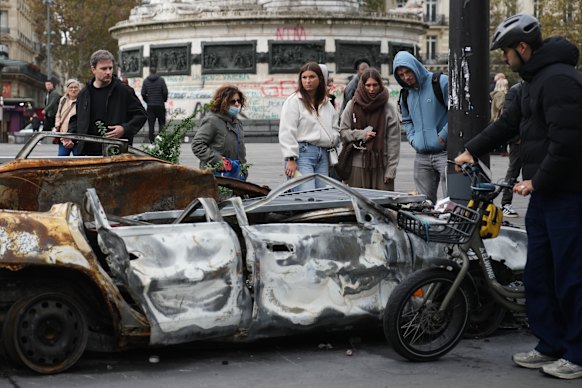People inspect the burnt-out remains of a car on Tuesday after a quieter night in the French capital.
