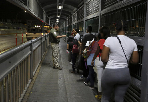 A Mexican immigration officer gives instructions to migrants who are applying for asylum in the US as they wait on the bridge to cross from Nuevo Laredo in Mexico to Laredo, Texas.