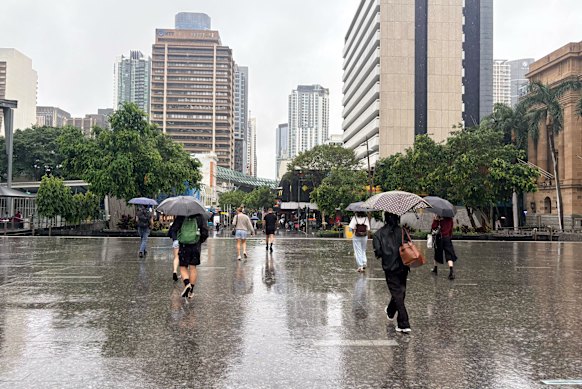 Pedestrians in inner-city Brisbane have their umbrellas out as rain falls throughout the city.
