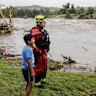 Patricio Levesange, left, his grandson, 10-year-old Benjamin Levesange, center, and a Kerrville Fire Department first responder scan the banks of the Guadalupe River for people swept away by flooding on Friday, July 4, 2025, in Ingram, Texas. (Michel Fortier/The San Antonio Express-News via AP)