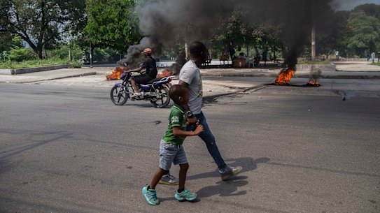 A man and a child walk by burning tires on a street on Sunday in Port-au-Prince, Haiti, where a group of 17 US missionaries, including children, was kidnapped by a gang.