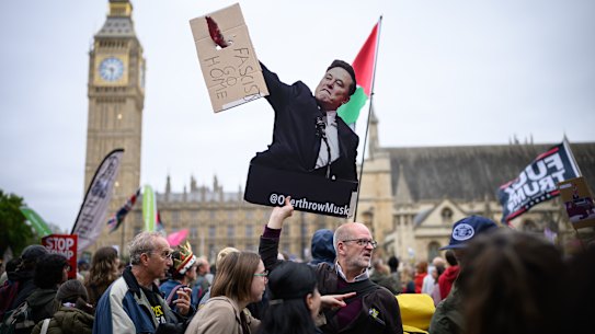 A man holds a cardboard cutout of Elon Musk at a UK protest.
