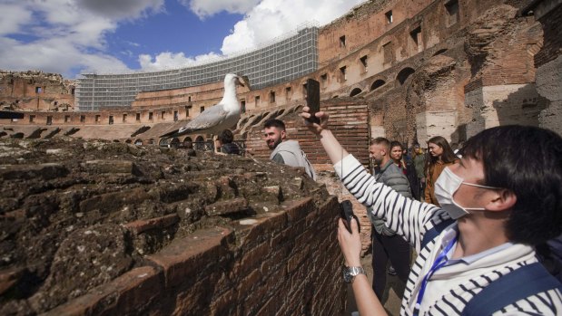 A tourist wearing a mask takes a photo at the Colosseum in Rome.