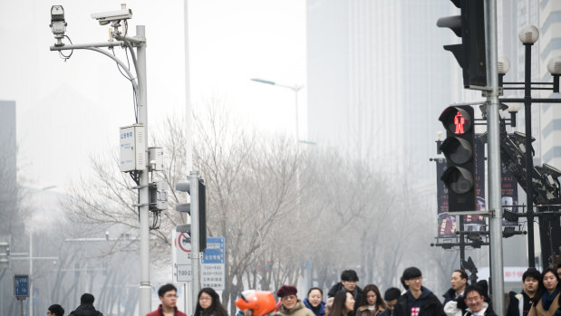 Pedestrians wait to cross a road as surveillance cameras operate in Tianjin, China.