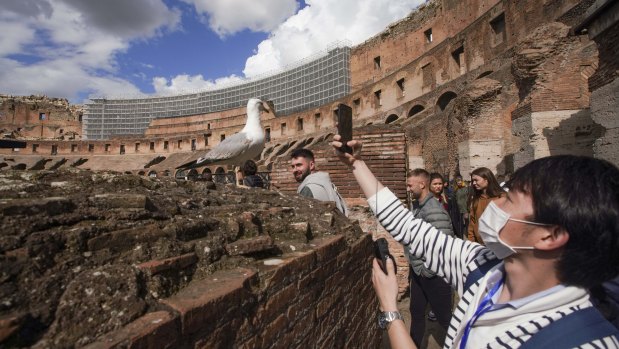 A tourist wearing a mask takes a photo at the Colosseum in Rome on Saturday. 