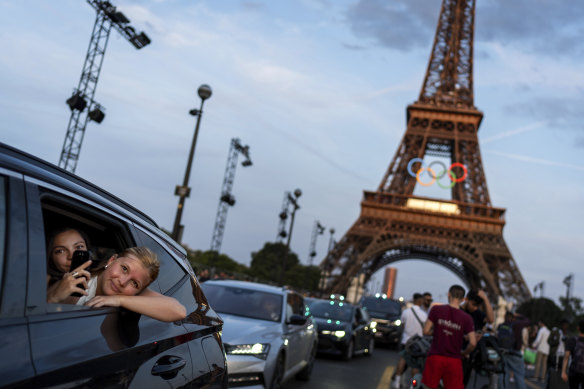 Passengers in the back of a taxi film themselves as they leave the Eiffel Tower decorated with the Olympic rings ahead of the 2024 Summer Olympics in Paris.