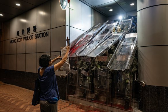 A woman holds a cross in front of the Mongkok Police Station as riot police holding shields stand guard during a standoff with protesters after an anti-government rally in on September 1, 2019 in Hong Kong.