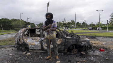 A man stands in front of a burnt car after unrest in Noumea, New Caledonia this week.