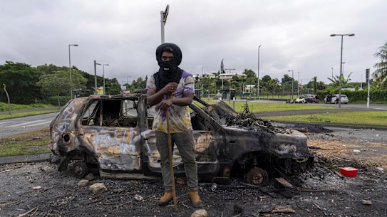 A man stands in front of a burnt car after unrest in Noumea, New Caledonia this week.