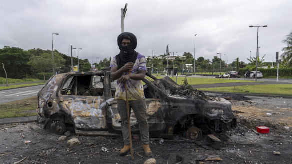 A man stands in front of a burnt car after unrest in Noumea, New Caledonia this week.
