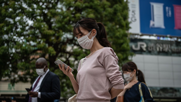 People wearing face masks wait to walk over Shibuya crossing in Tokyo, Japan. 