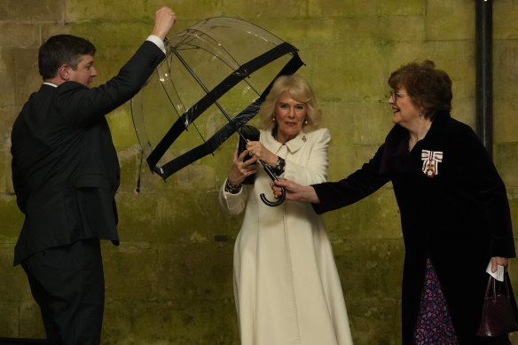 Queen Camilla hands her umbrella to an aide as she arrives to attend a musical evening at Salisbury Cathedral.