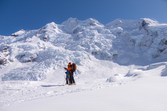 Guide Sean Brooks pointing out the peaks with the ice of a hanging glacier in the background.