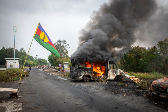 A Kanak flag waving next to a burning vehicle at a roadblock at La Tamoa, in the commune of Paita in New Caledonia.