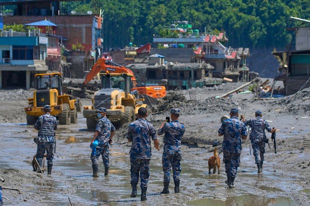 Nepal'in Nuwakot bölgesinde sel sonrası molozları temizleyen iş makinelerini izleyen Nepal polisleri.