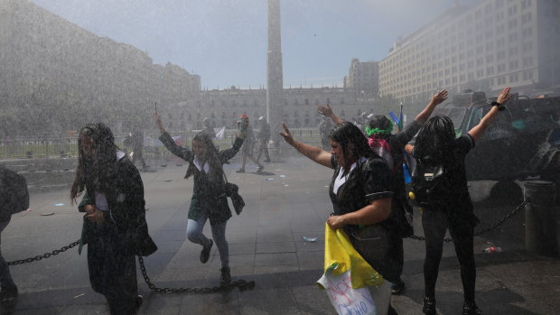 Anti-government protesters gleefully accept showers of water from a police water cannon that is meant to disperse them, outside La Moneda presidential palace in Santiago.