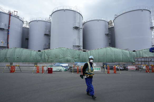 Bir işçi, Fukushima Daiichi nükleer santralinde erimiş yakıtı soğutmak için kullanıldıktan sonra arıtılmış radyoaktif suyu depolamak için kullanılan tankların yanında duran bir kamyon şoförünü yönlendirmeye yardım ediyor.
