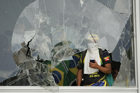 Protesters, supporters of Brazil’s former president Jair Bolsonaro, look out from a shattered window after they storm the Planalto Palace in Brasilia.