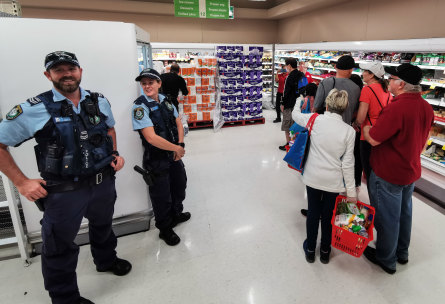Police officers watch as people queue at a Coles supermarket in Epping, Sydney.