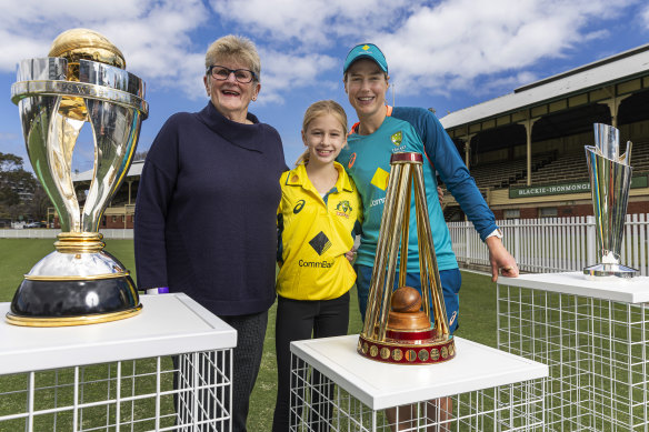 Former Australian World Cup cricketer Margaret Jennings, junior fan Annabel Archer, and Ellyse Perry from the current Australian cricket team pose for a photograph with the ICC World Cup, Ashes and ICC T20 trophies. 