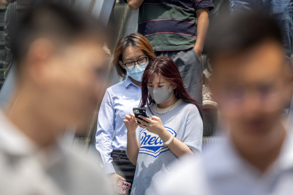 People wearing face masks ride an escalator at a shopping and office complex in Beijing, 