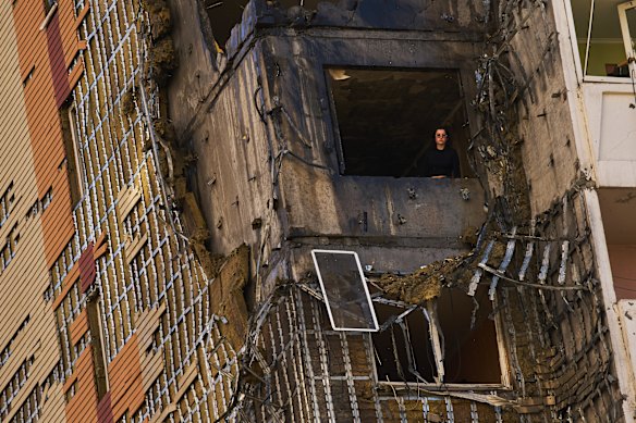 A woman looks out from a wrecked apartment in a residential building.