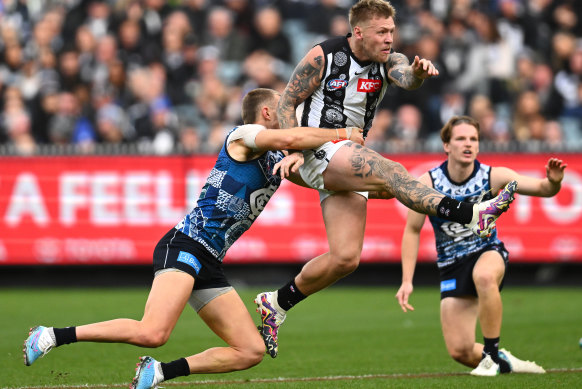 Jordan De Goey kicks while being tackled by Patrick Cripps.