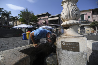 Un uomo cerca di rinfrescarsi presso una fontana dell'Ace Tresa, in Sicilia, dove le temperature raggiungono un nuovo record europeo.