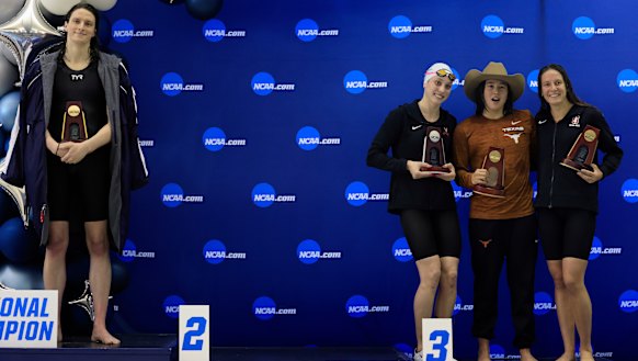 Lia Thomas (left) stands alone on the podium as the other placegetters pose for a group photo.