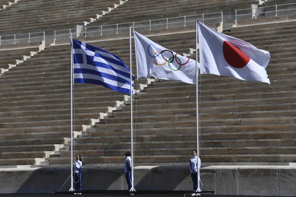 Athletes stand under the Greek, Olympic and Japanese flags during the Olympic flame handover ceremony for the Tokyo Summer Olympics in Athens in  March 2020.