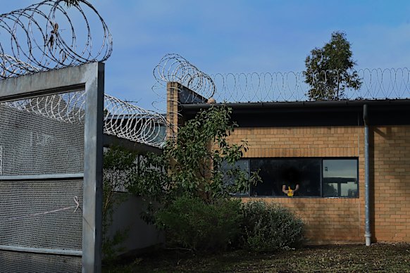 A young inmate holds a table tennis bat while looking out over the yard at Reiby Youth Justice Centre.