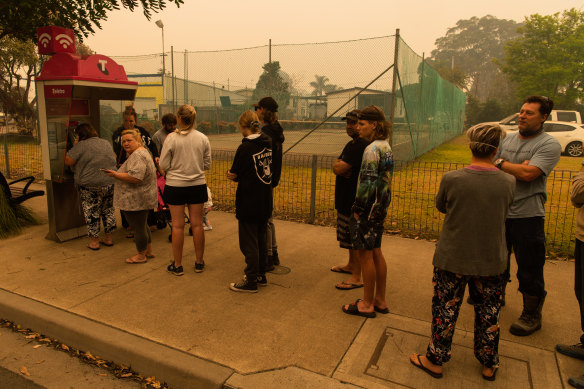 Displaced residents line up to use a payphone in Narooma.