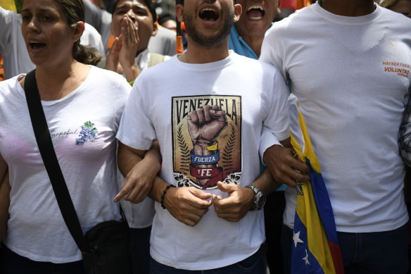 A man wearing a shirt that reads in Spanish "Venezuela. Strength and faith." links arms with others at an opposition rally in Caracas on Tuesday.