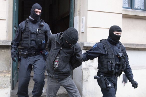 Police officers lead a suspect out of a building entrance during a raid in the Pieschen district in Dresden, Germany.