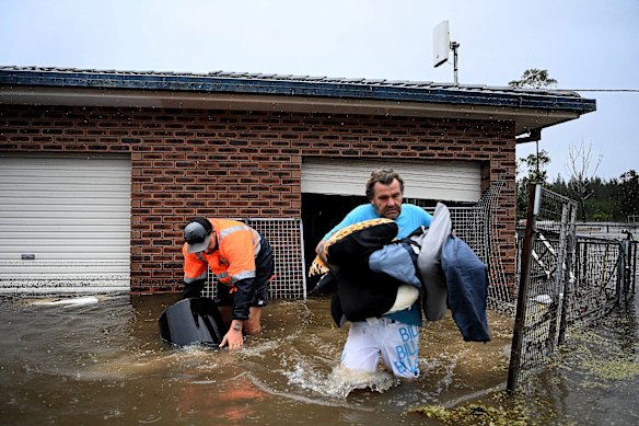 James Larking (right), with the help of Dylan Smith. evacuates his flooded home in Pampoolah.