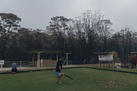 Residents of Lake Conjola help clean up the local bowling club, with burnt forrest just metres behind them.