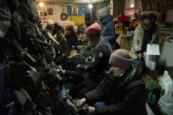 A group of women tie strips of donated material creating camouflage nets in a community shelter in Uman. 