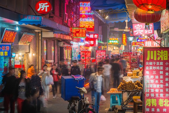 Neon signs illuminate a crowded and narrow hutong laneway in the heart of Beijing, China. 