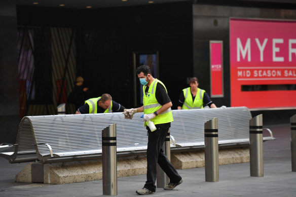 Benchmark: workers sanitising Bourke Street Mall benches in front of a closed Myer store.