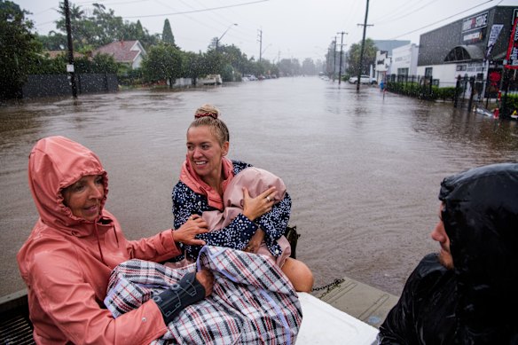 Abbie Bayliss with her daughter Cienna Cumming and mum Mel, getting a lift through floodwaters along Pittwater Road, North Manly, in the back of Freshwater local Nick Fraser’s truck.