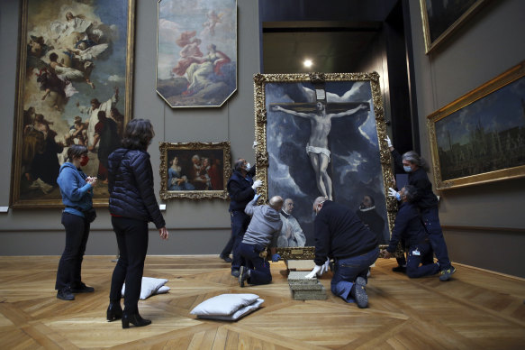 Workers handle a painting called ‘Christ on the Cross Adored by Two Donors’ by Spanish painter El Greco amid works at the Louvre.