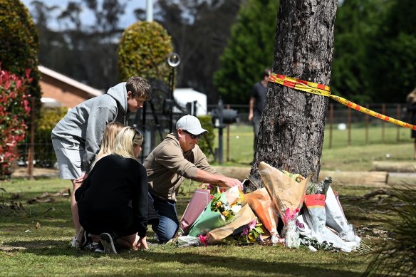 A family places a framed photo at the base of a tree where five young people were killed in a crash on Tuesday night on East Parade in Buxton, NSW.