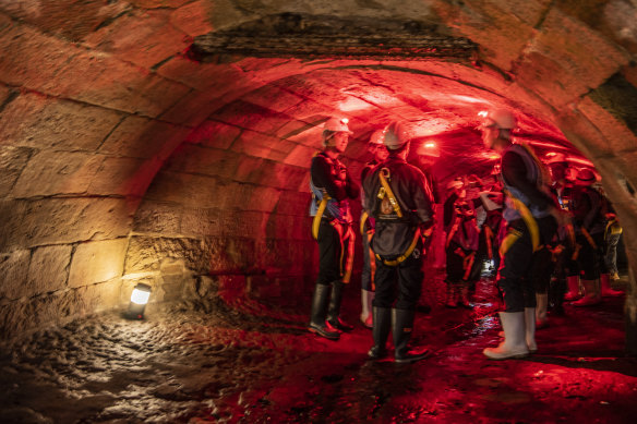 A tour group navigates through the Tank Stream, a heritage-listed stormwater tunnel under Sydney's CBD. 